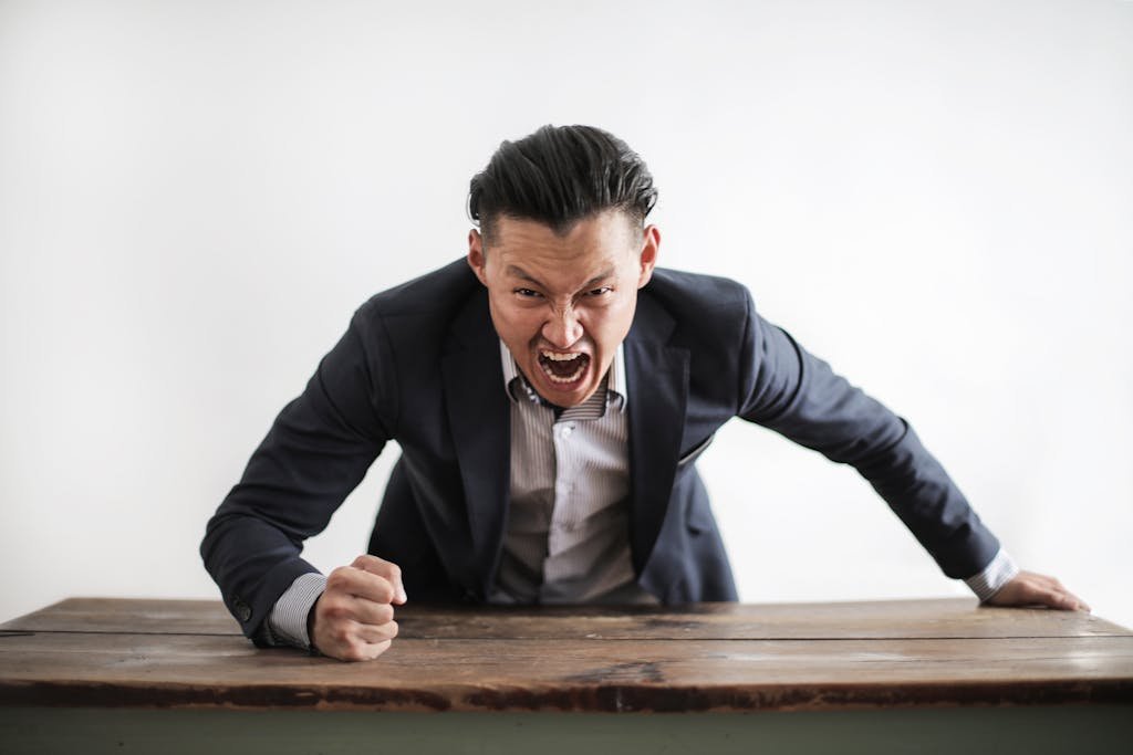 Homme en colère, criant et frappant du poing sur une table en bois, expression agressive resilience-pn.com