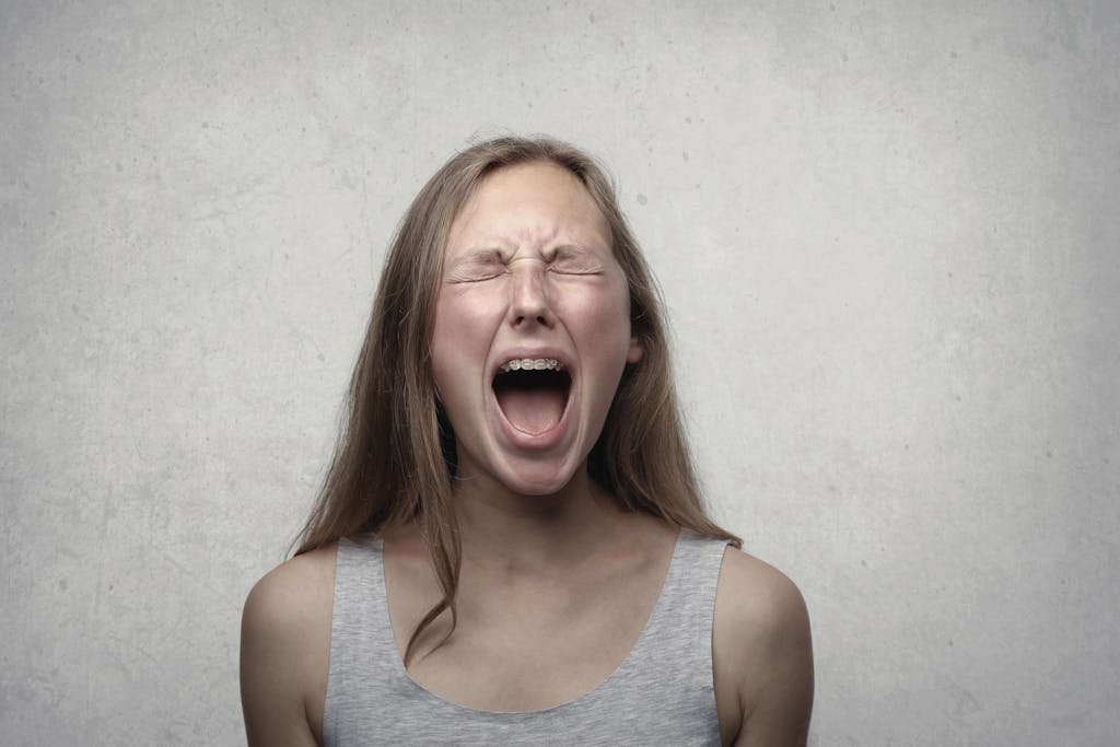 Femme aux yeux fermés criant intensément, expression de colère extrême, cheveux longs resilience-pn.com